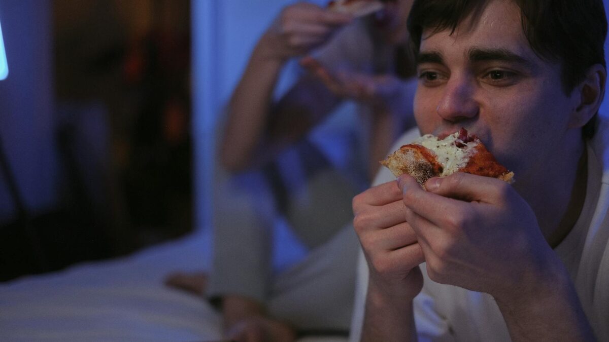 Pessoa comendo lanches à noite com expressão de estresse, ilustrando os efeitos negativos para a saúde digestiva
