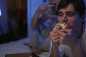 Pessoa comendo lanches à noite com expressão de estresse, ilustrando os efeitos negativos para a saúde digestiva