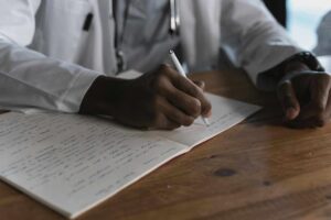 Médico revendo anotações num consultório, com computador visível à mesa
