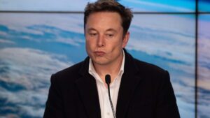 Elon Musk em primeiro plano com logos do OpenAI e Tesla ao fundo, ilustrando a tentativa de aquisição revelada no julgamento de 2026